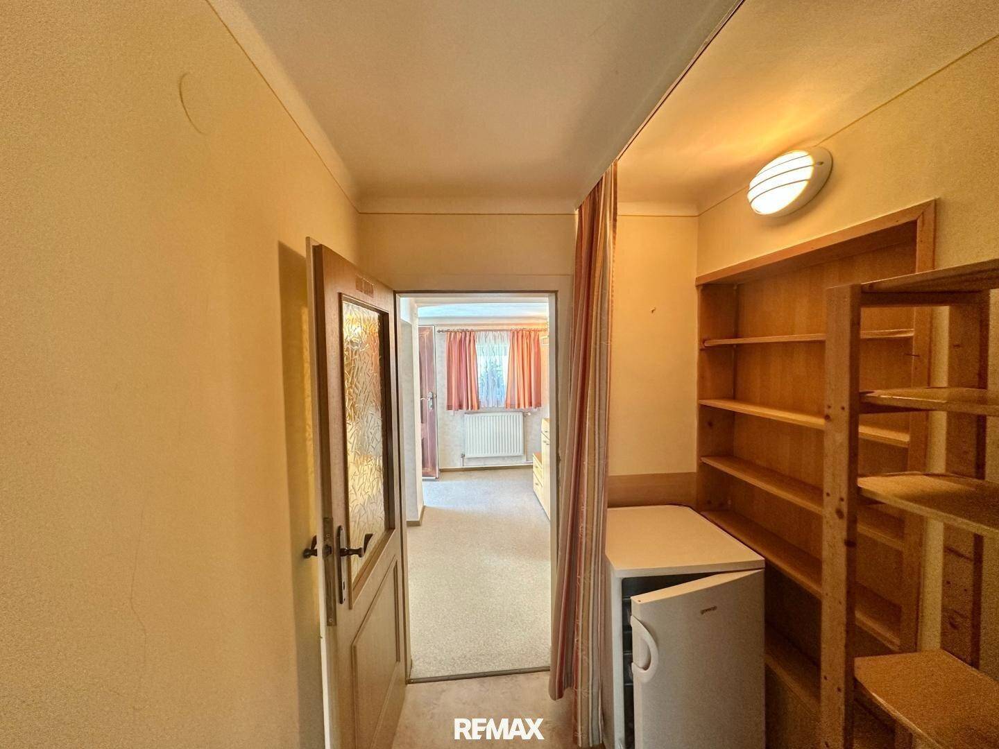 Praktischer Abstellraum mit Holzregalen und kleinem Kühlschrank, der zusätzlichen Stauraum bietet.