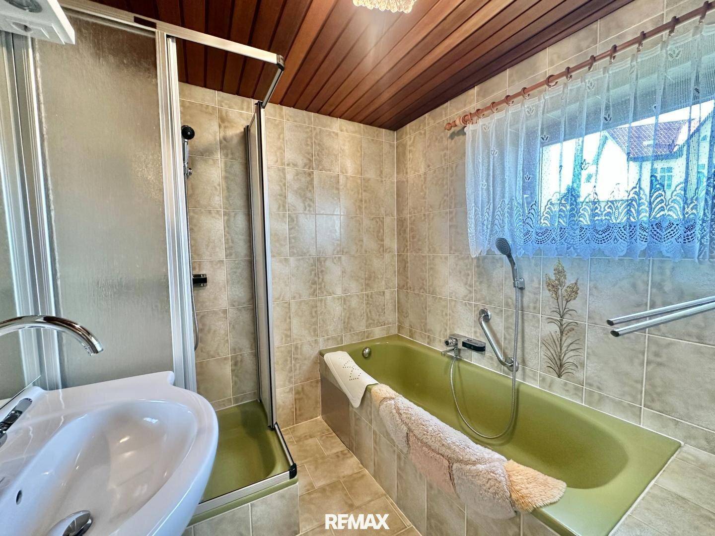 Helles Badezimmer mit Duschkabine, grüner Badewanne und Fenster, das für natürliche Belüftung sorgt.