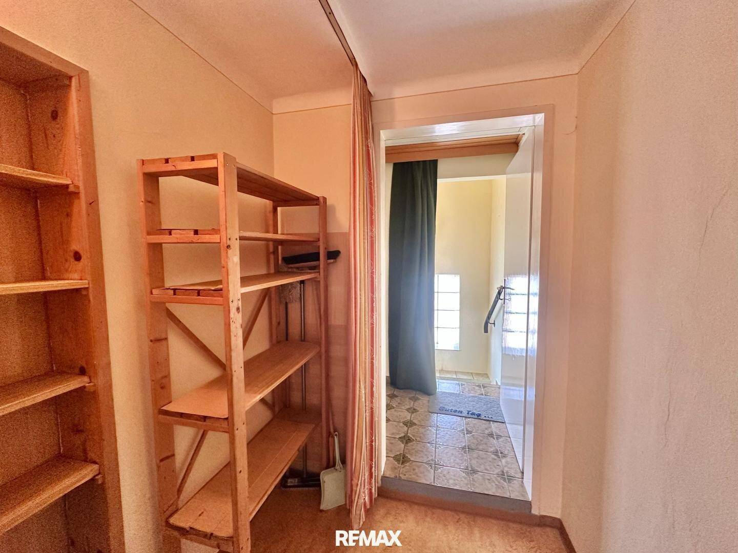 Abstellraum mit einfachen Holzregalen und Zugang zu einem gefliesten Bereich mit Treppe.