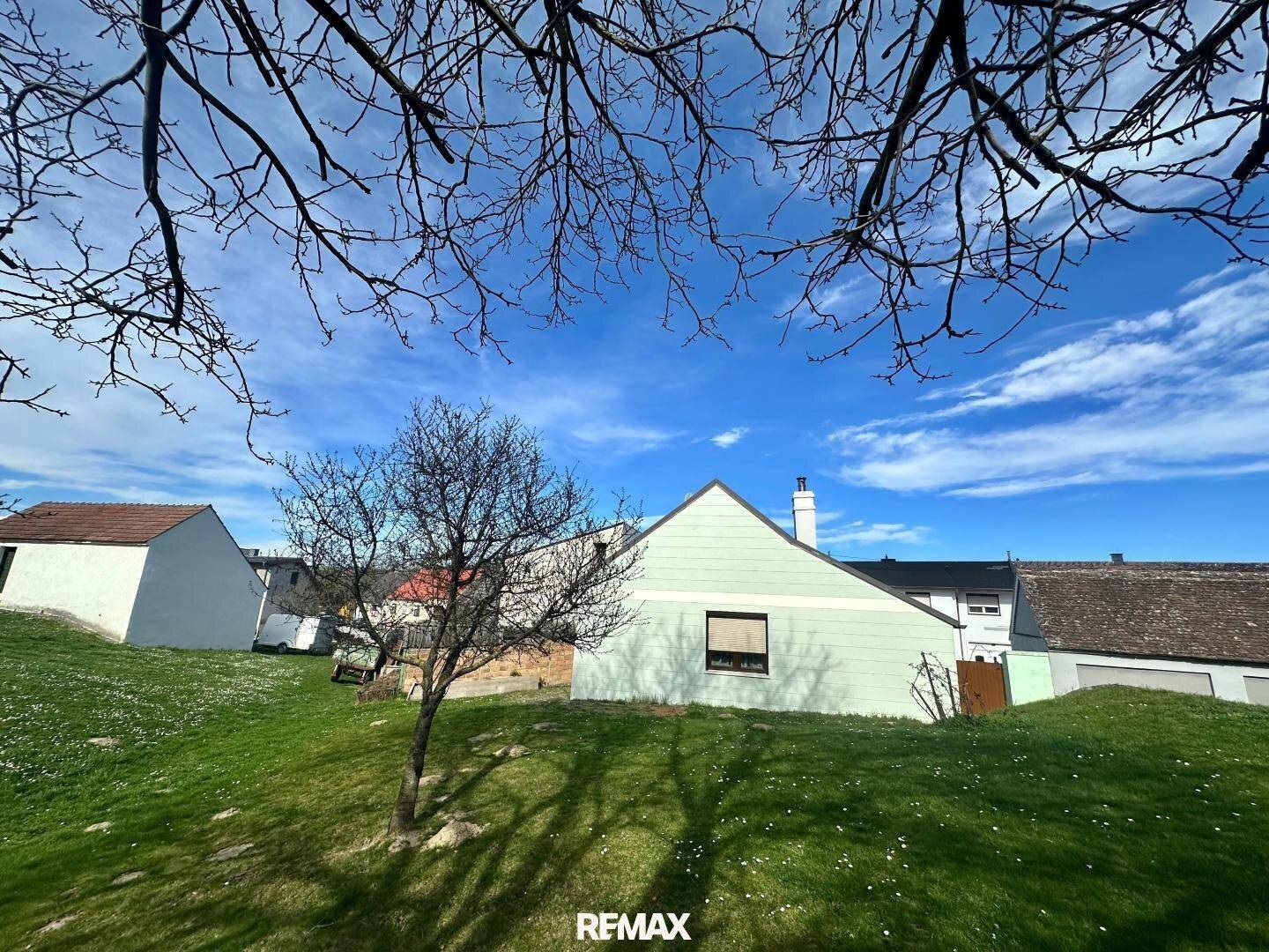 Rückansicht des Hauses mit Satteldach und weitläufiger Grünfläche unter blauem Himmel.