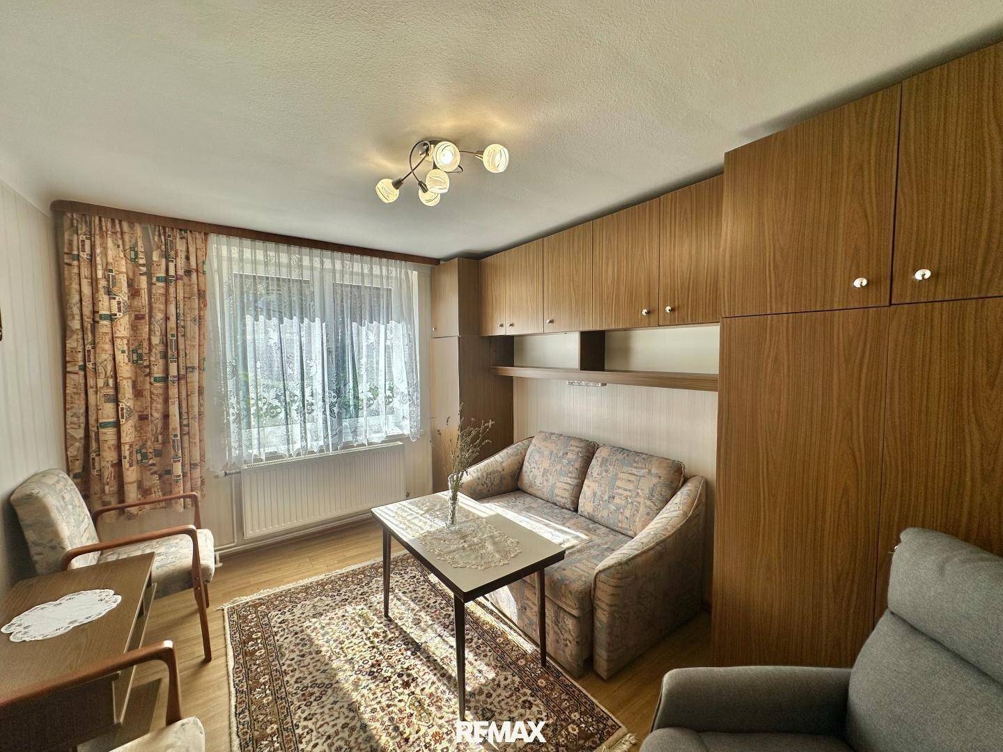 Gemütliches Wohnzimmer mit Sofa, Sesseln und integrierten Holzschränken, die viel Stauraum bieten.