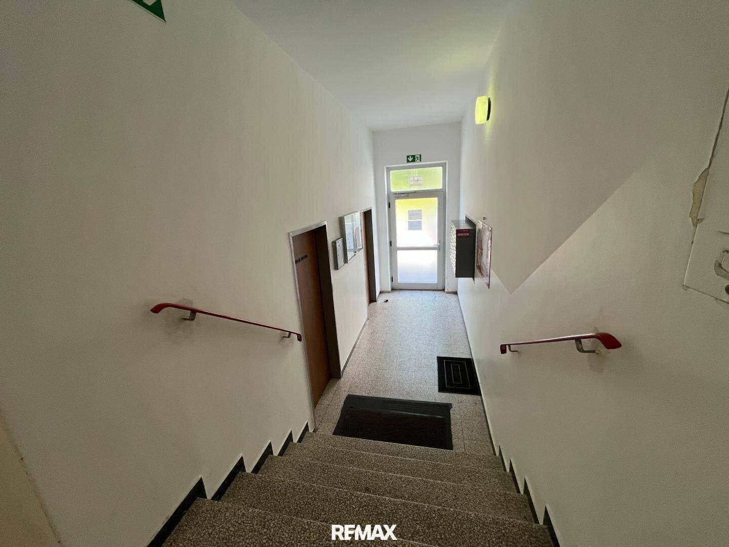 Treppenhaus mit Fliesenstufen und Handläufen, das zum Ausgang des Gebäudes führt.