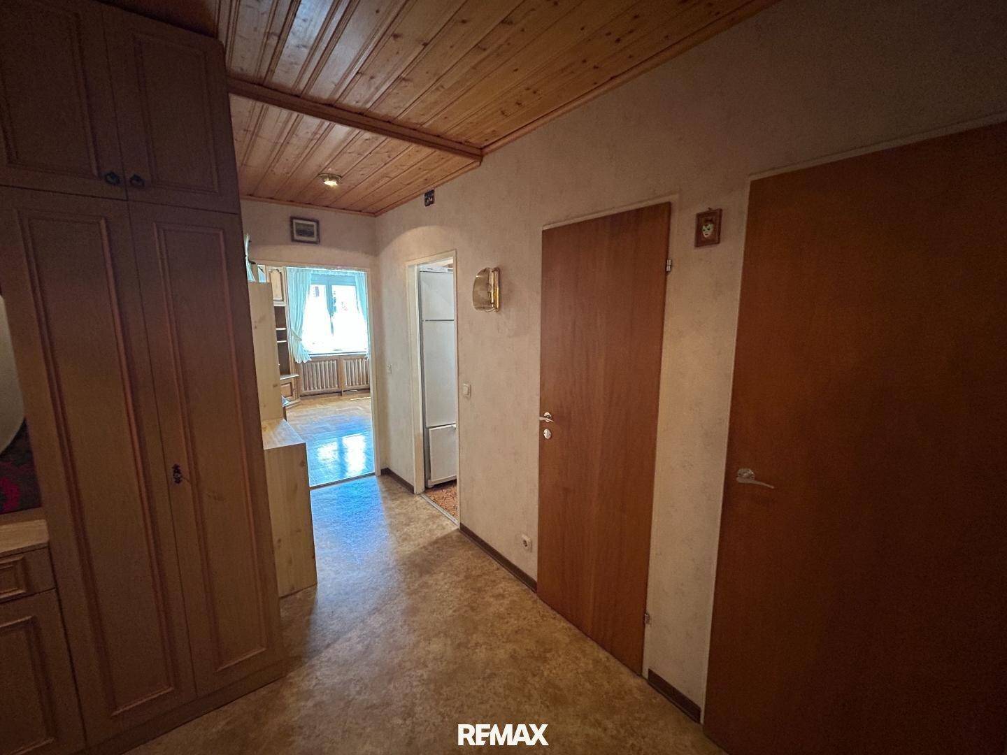 Flur mit Einbauschrank und Zugang zu weiteren Räumen, mit Holzdecke und Fliesenboden.