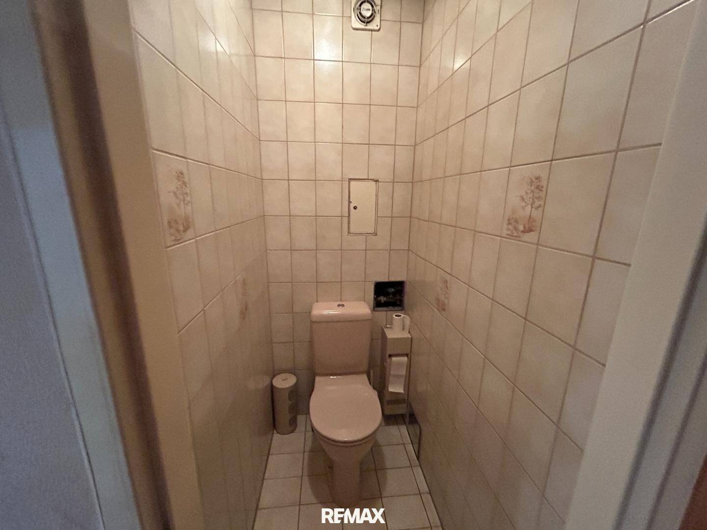 Separates WC mit hellen Fliesen an Wänden und Boden, funktional und sauber.