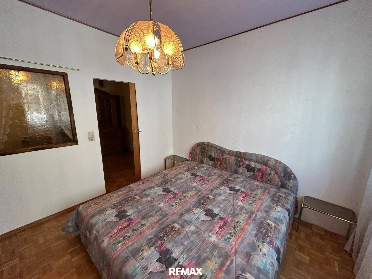 Geräumiges Schlafzimmer mit Parkettboden und Zugang zu weiteren Räumen, mit gemütlicher Beleuchtung.