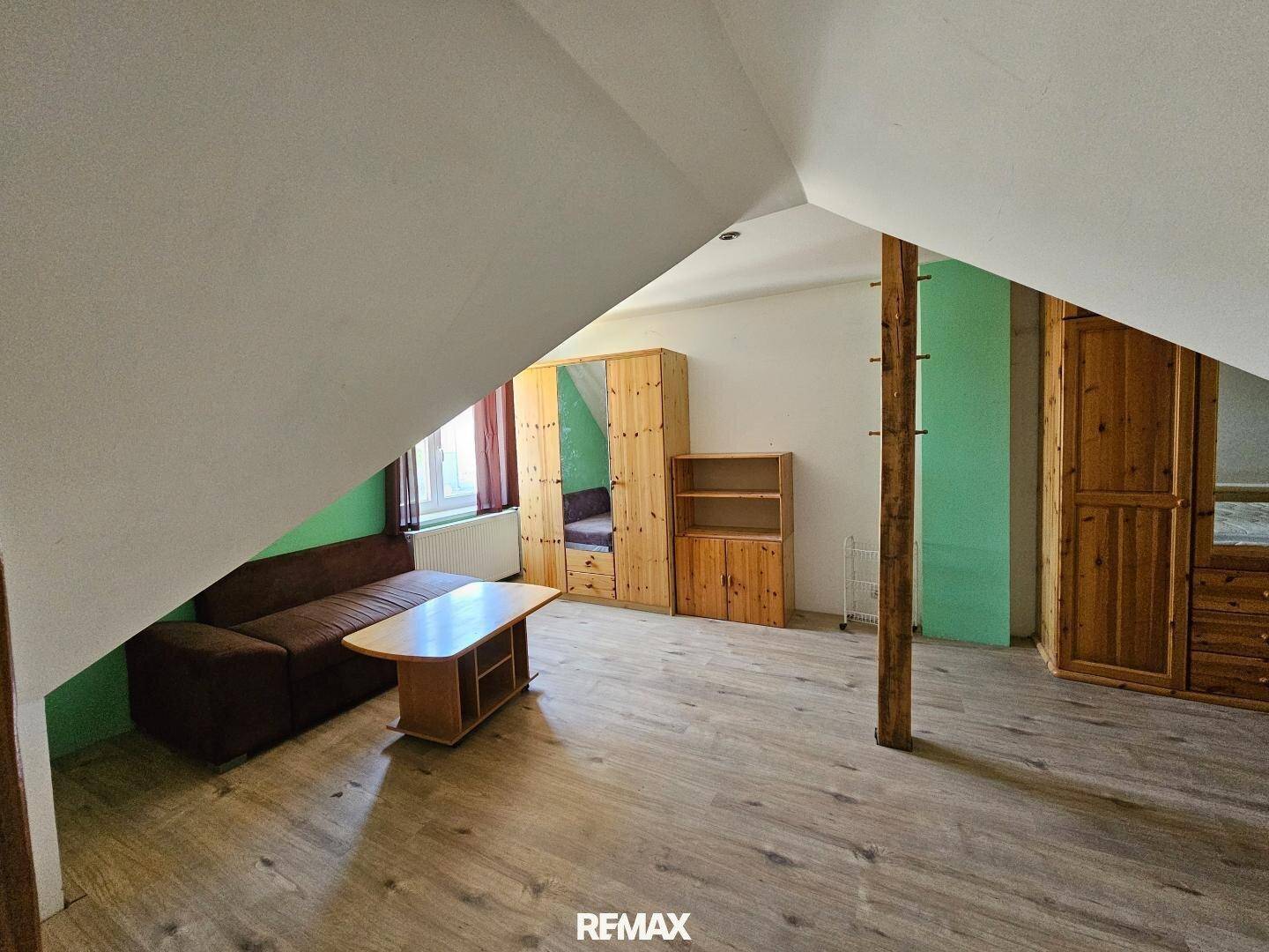 Dachgeschosszimmer mit schrägen Wänden, Holzbalken und Laminatboden.