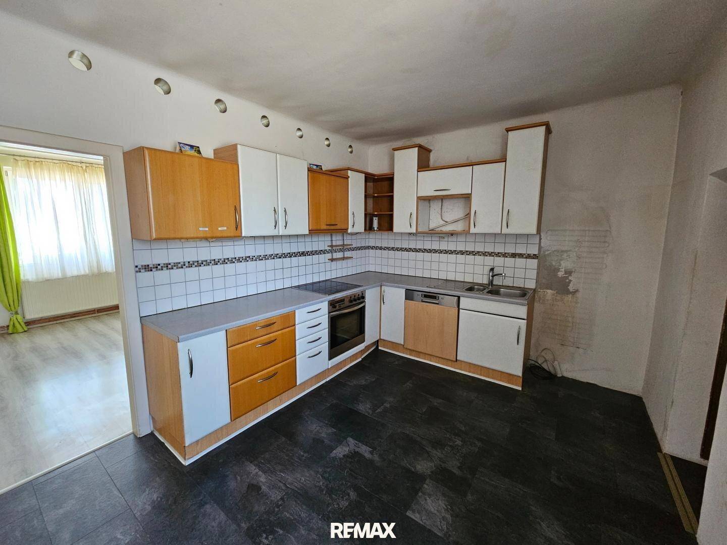 Geräumige Küche mit L-förmiger Küchenzeile, Holzschränken und dunklem Fliesenboden.