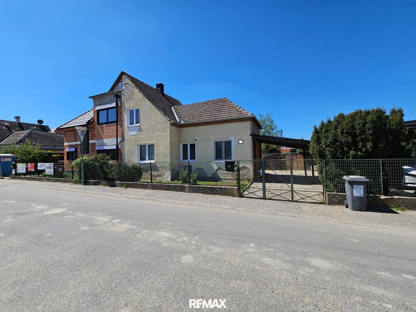 Weitläufige Ansicht des Hauses von der Straße mit Vorgarten und klarem Himmel.