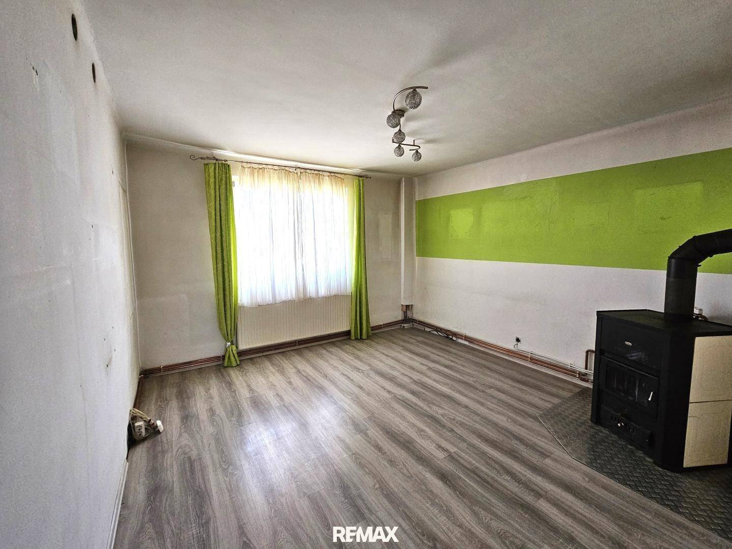 Wohnzimmer mit Laminatboden, grünem Wandstreifen und Holzofen als Heizquelle.