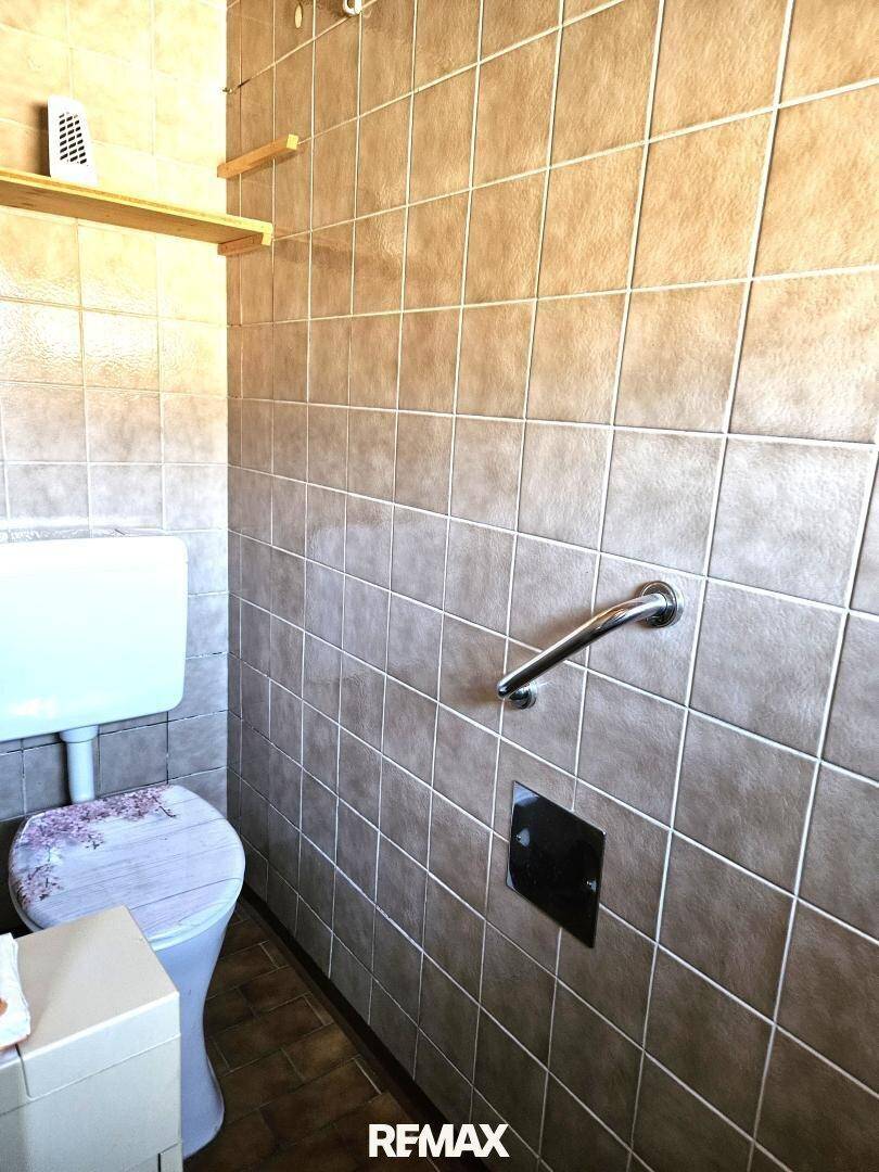 Toilette mit braunen Fliesen, Wand-WC und Haltegriff für zusätzliche Sicherheit.