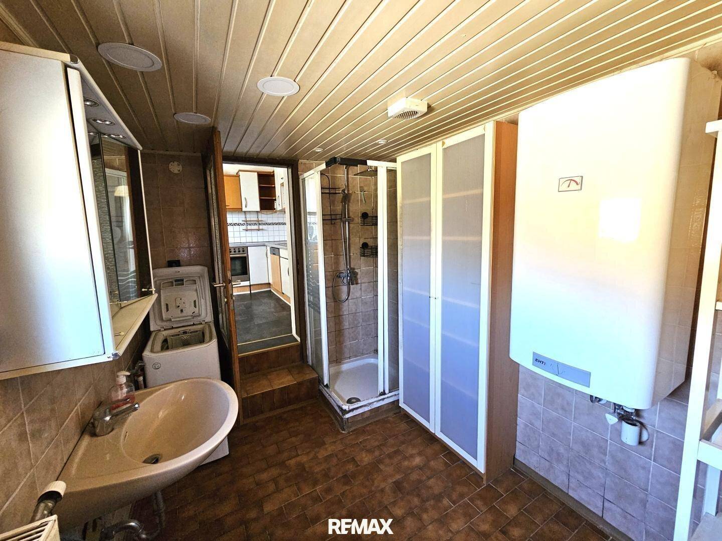 Geräumiges Badezimmer mit Dusche, Waschmaschine und Warmwasserboiler.