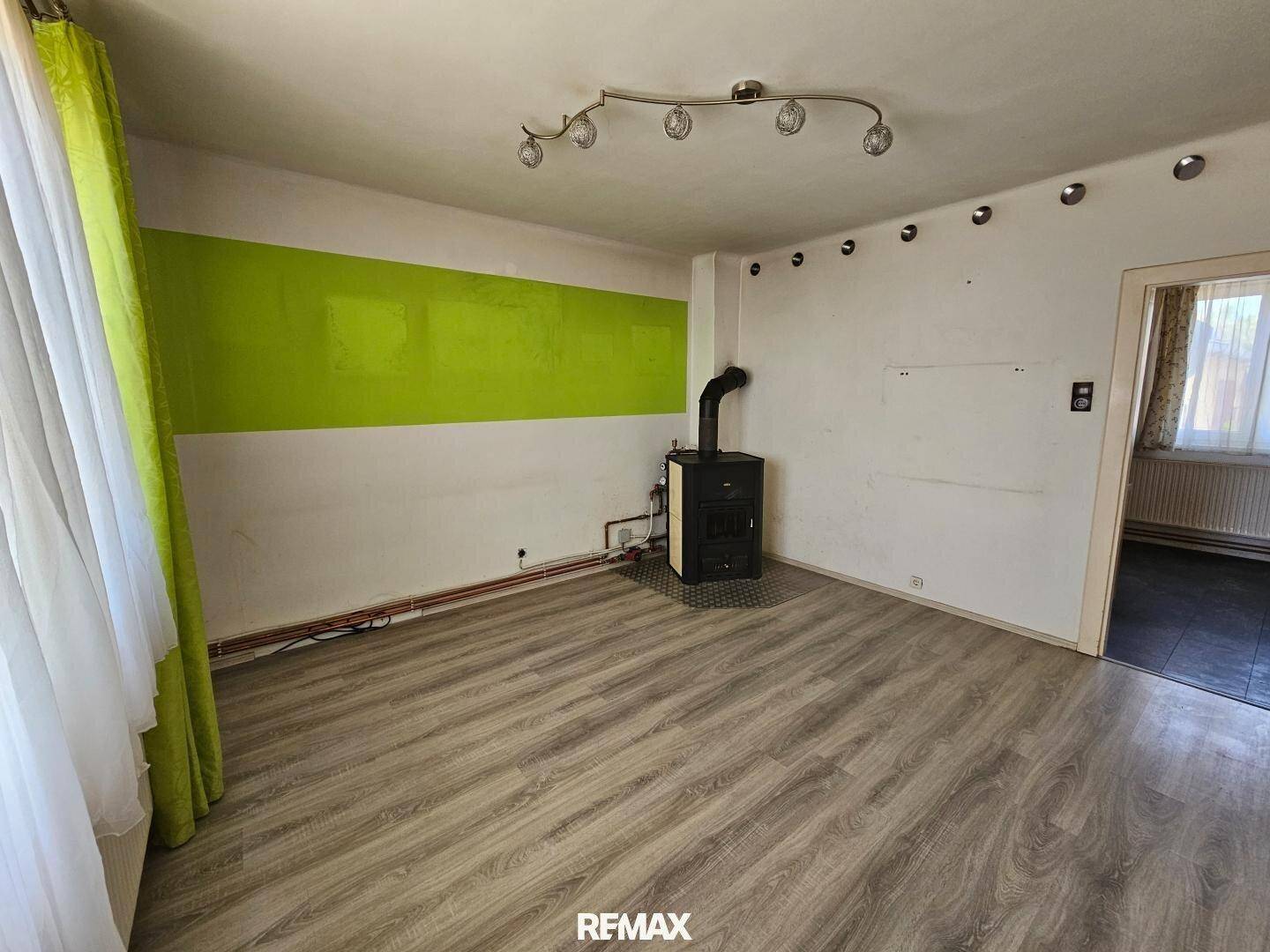 Heller Wohnbereich mit Laminatboden, grünem Akzent und Kaminofen für gemütliche Abende.