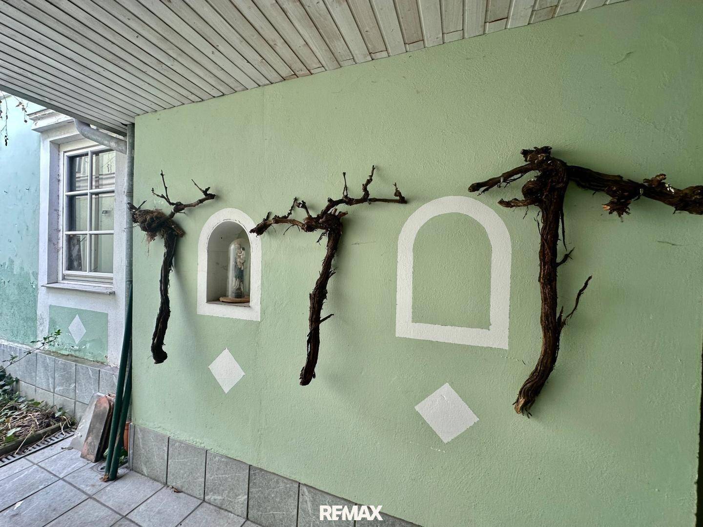 Überdachter Außenbereich mit grüner Wand und dekorativen Nischen, geschmückt mit Weinstockranken.