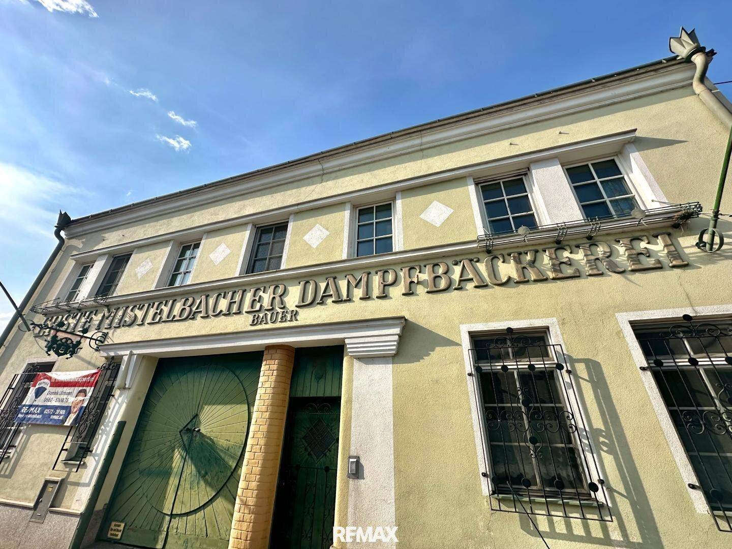 Historische Fassade einer ehemaligen Dampfbackerei mit großen Fenstern und grüner Eingangstür.