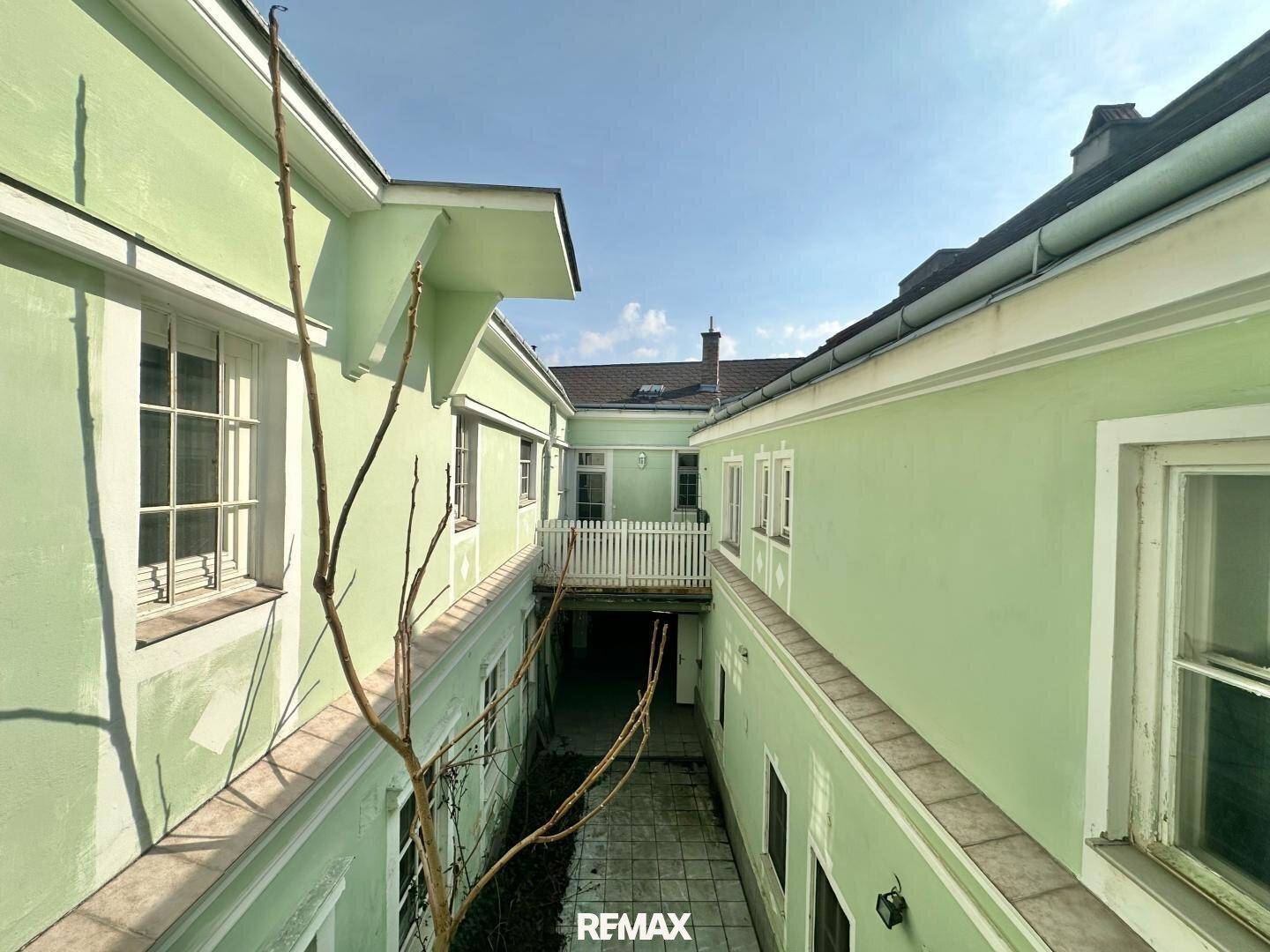 Blick in einen hellgrünen Innenhof mit schmalem Durchgang und Fenstern.