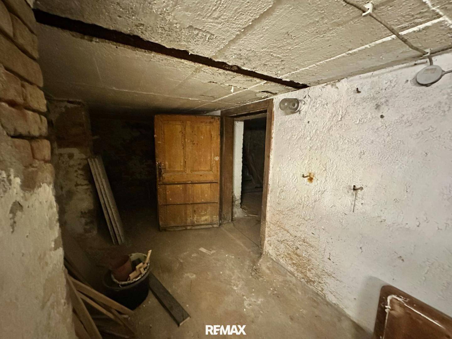 Einfacher Kellerraum mit einer alten Holztür und unebenen Wänden, bietet zusätzlichen Stauraum.