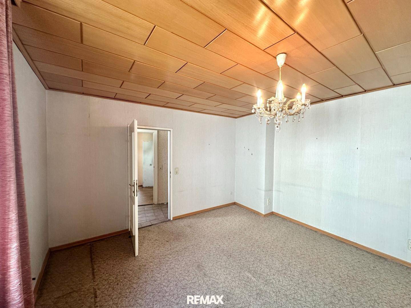 Geräumiges Zimmer mit Holzbalkendecke, Teppichboden und Kronleuchter.