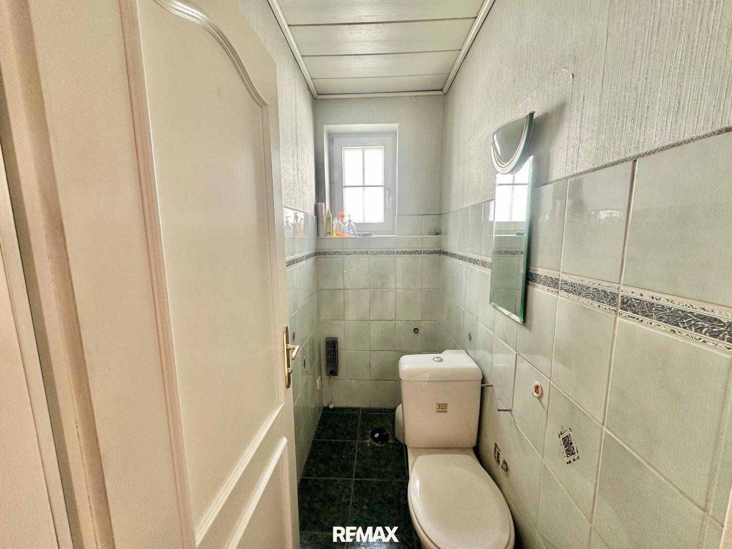 Separate Toilette mit Fenster, Wandfliesen und einfacher Ausstattung.