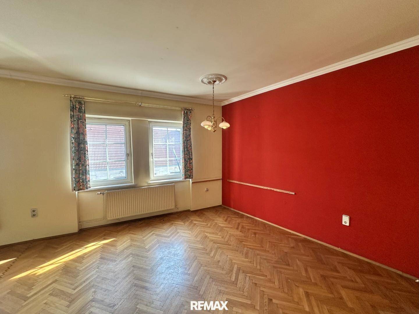 Helles Wohnzimmer mit Fischgrätparkett, roter Wand und großen Fenstern.