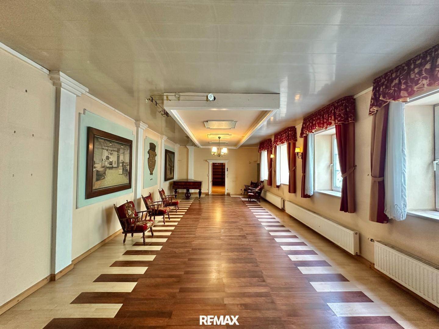 Langer, eleganter Saal mit Holzboden, hohen Decken und traditionellen Wandleuchten, ideal für Empfänge.