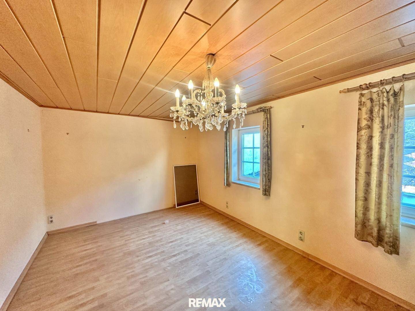 Geräumiges Zimmer mit Holzbalkendecke, Parkettboden und Kronleuchter.