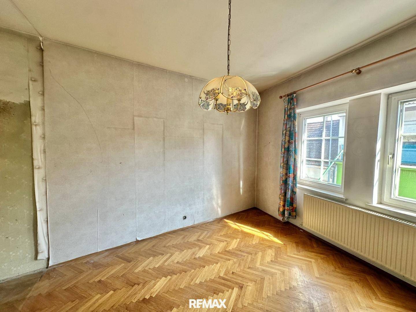 Helles Schlafzimmer mit Fischgrätparkett, großen Fenstern und Renovierungsbedarf.