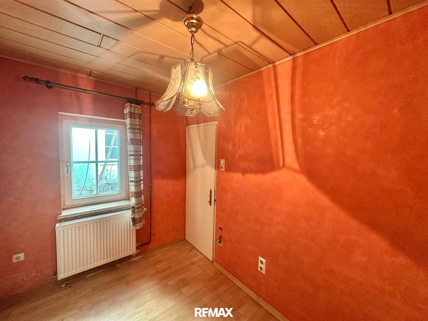 Gemütliches Zimmer mit roter Wandfarbe, Holzboden und Fenster, bietet Potenzial zur Gestaltung.