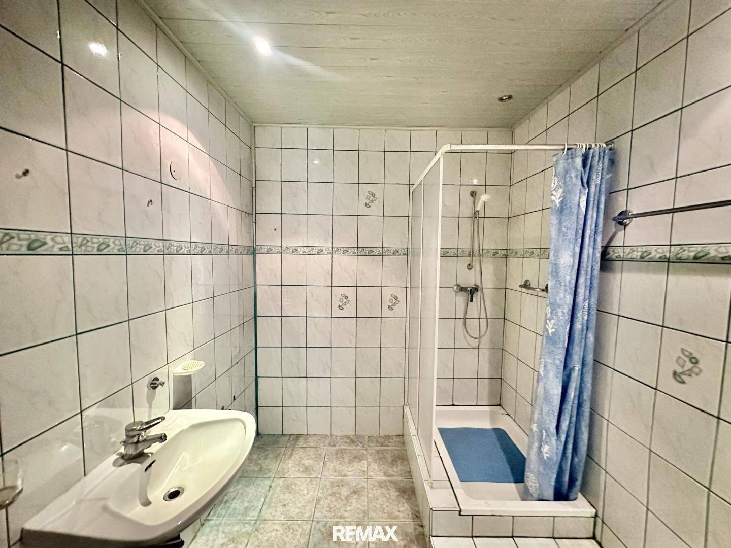 Badezimmer mit Duschkabine, Fliesenwänden und Waschbecken, funktional und hell.