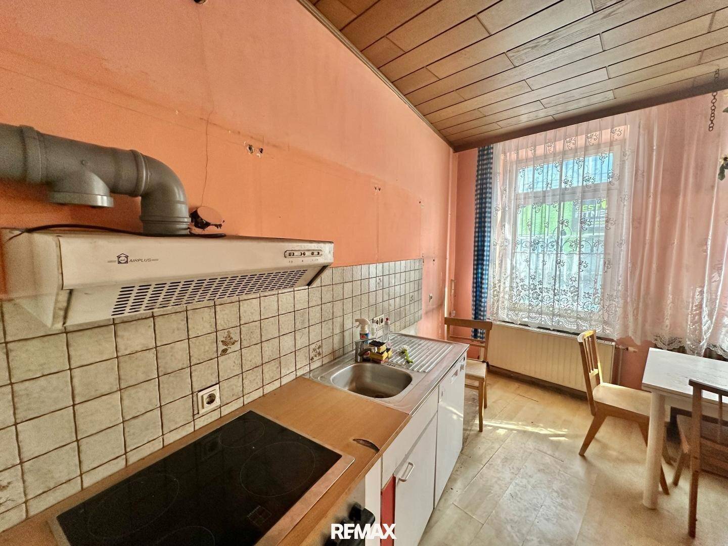 Einfache Küche mit Spüle, Kochfeld und Dunstabzugshaube, bereit für eine Modernisierung.