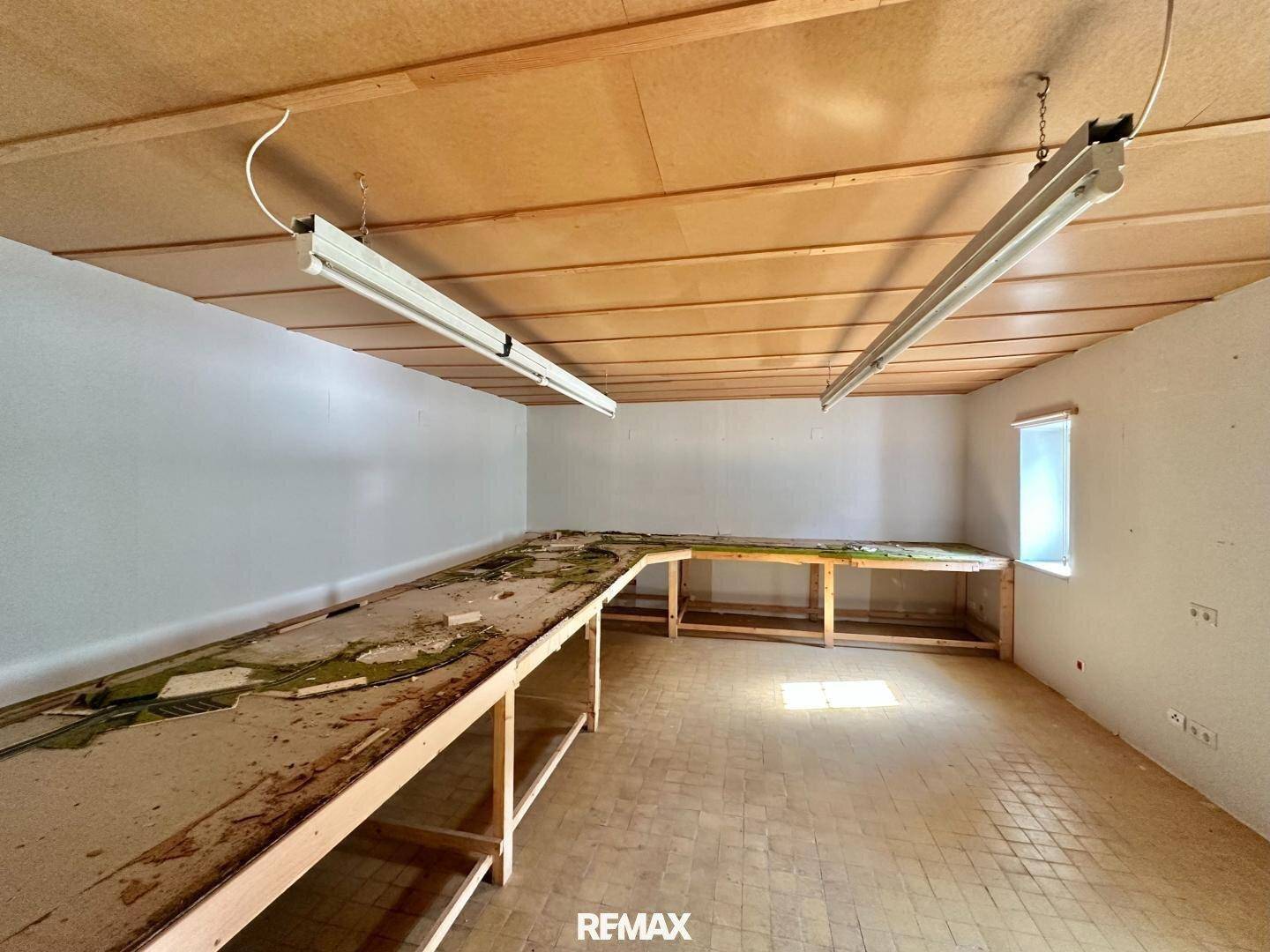 Großer Werkstattraum mit langen Arbeitstischen, Fliesenboden und Holzdecke.