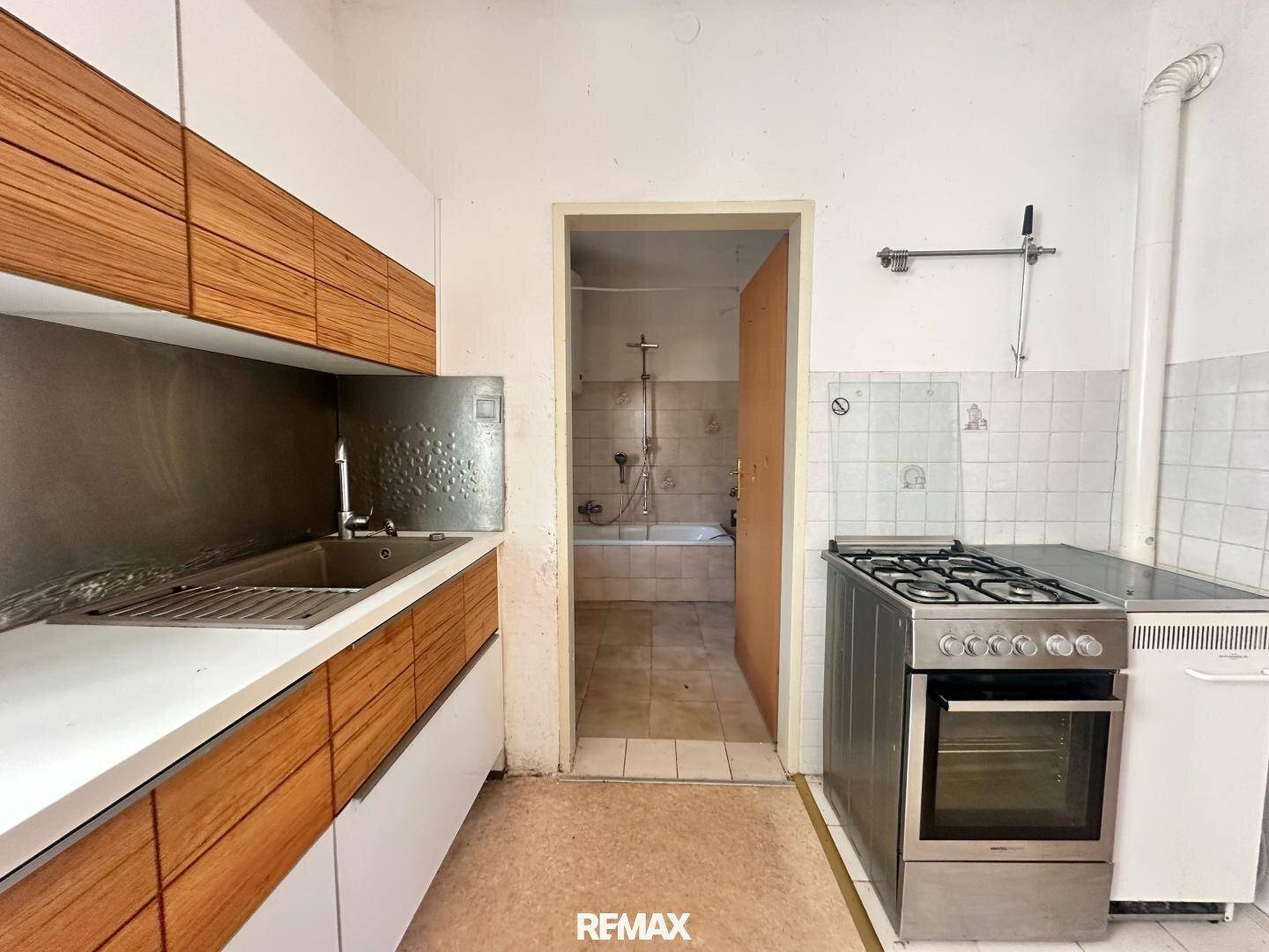 Küche mit Holzfronten, Gasherd und Blick in ein angrenzendes Badezimmer mit Badewanne.