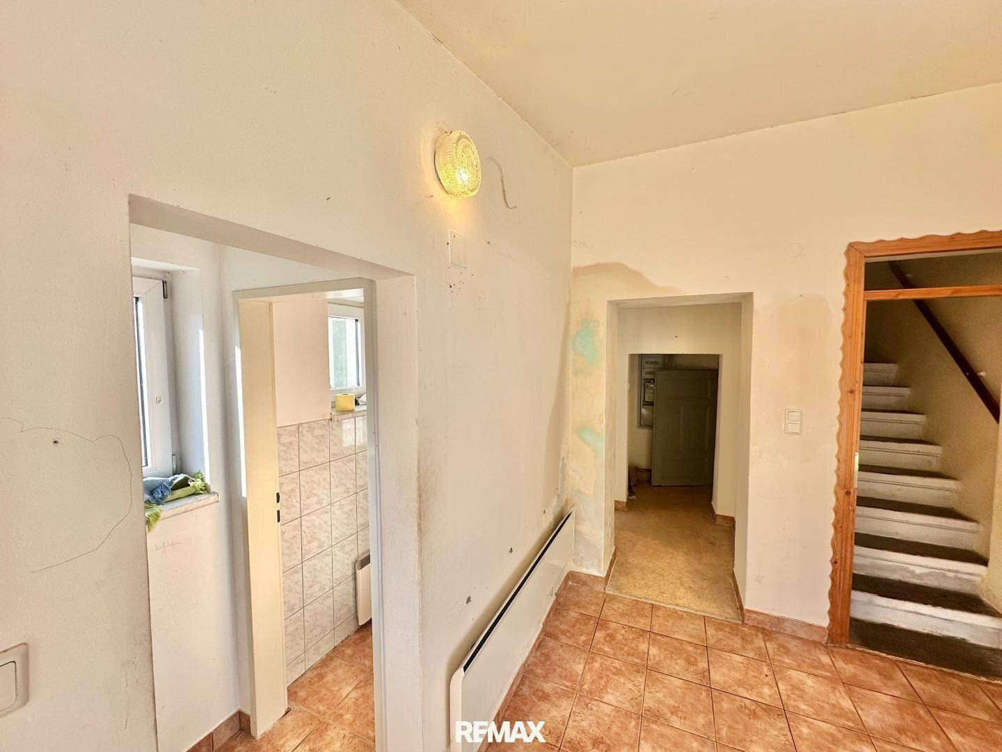 Heller Flur mit Fliesenboden, Heizkörper und Zugang zu weiteren Räumen und einer Treppe.