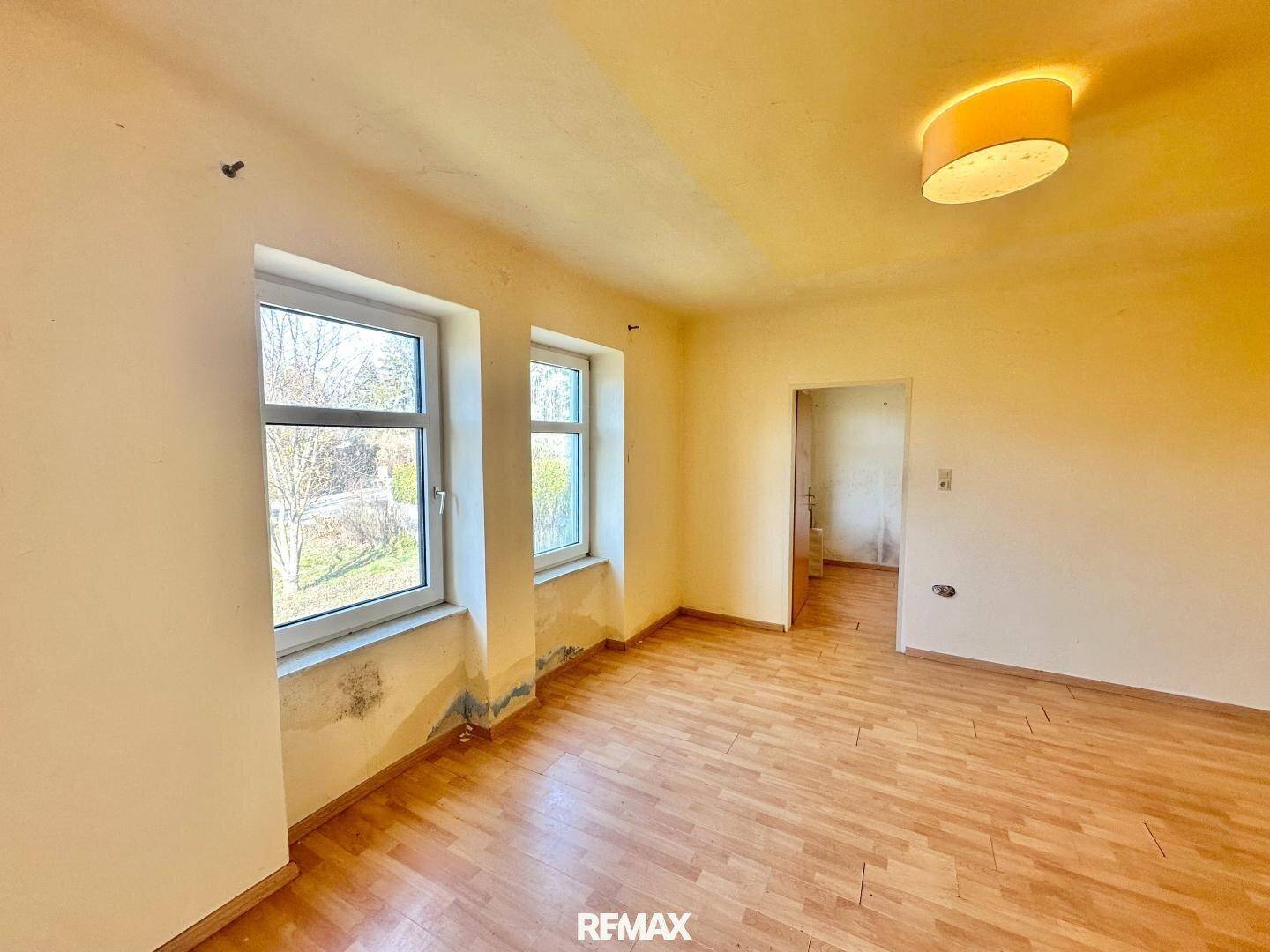 Wohnzimmer mit Parkettboden und zwei Fenstern, die einen Blick nach draußen ermöglichen.