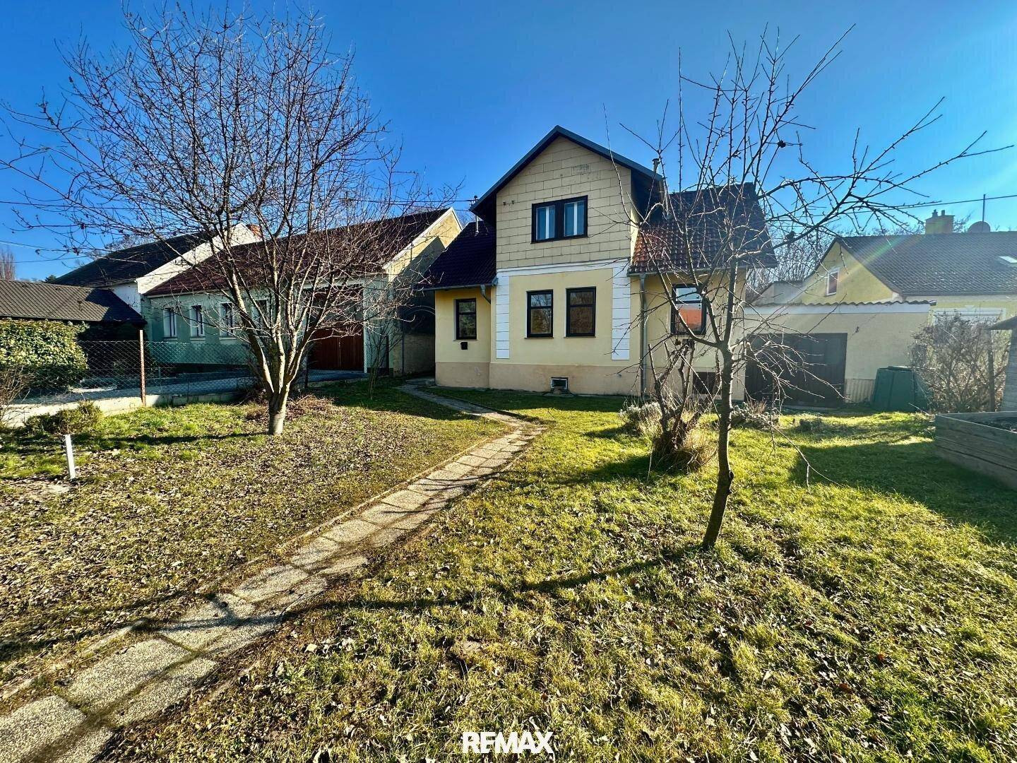 Vorderansicht des Hauses mit einem gepflasterten Weg und einer weitläufigen Rasenfläche.