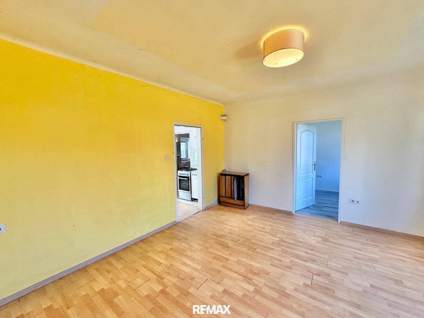 Geräumiges Wohnzimmer mit Parkettboden, einer gelben Akzentwand und Zugang zu weiteren Räumen.