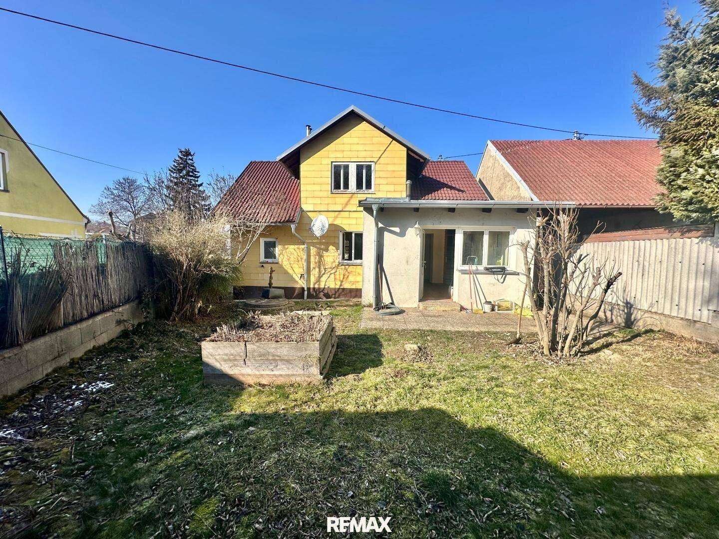 Gartenbereich mit einem gelben Haus im Hintergrund und einem Hochbeet im Vordergrund.