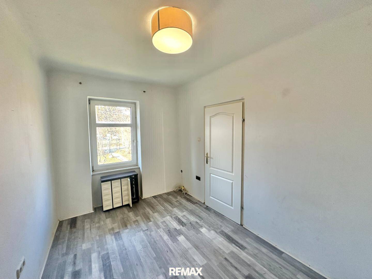 Helles Zimmer mit modernem Laminatboden und einem Fenster, das viel Tageslicht hereinlässt.