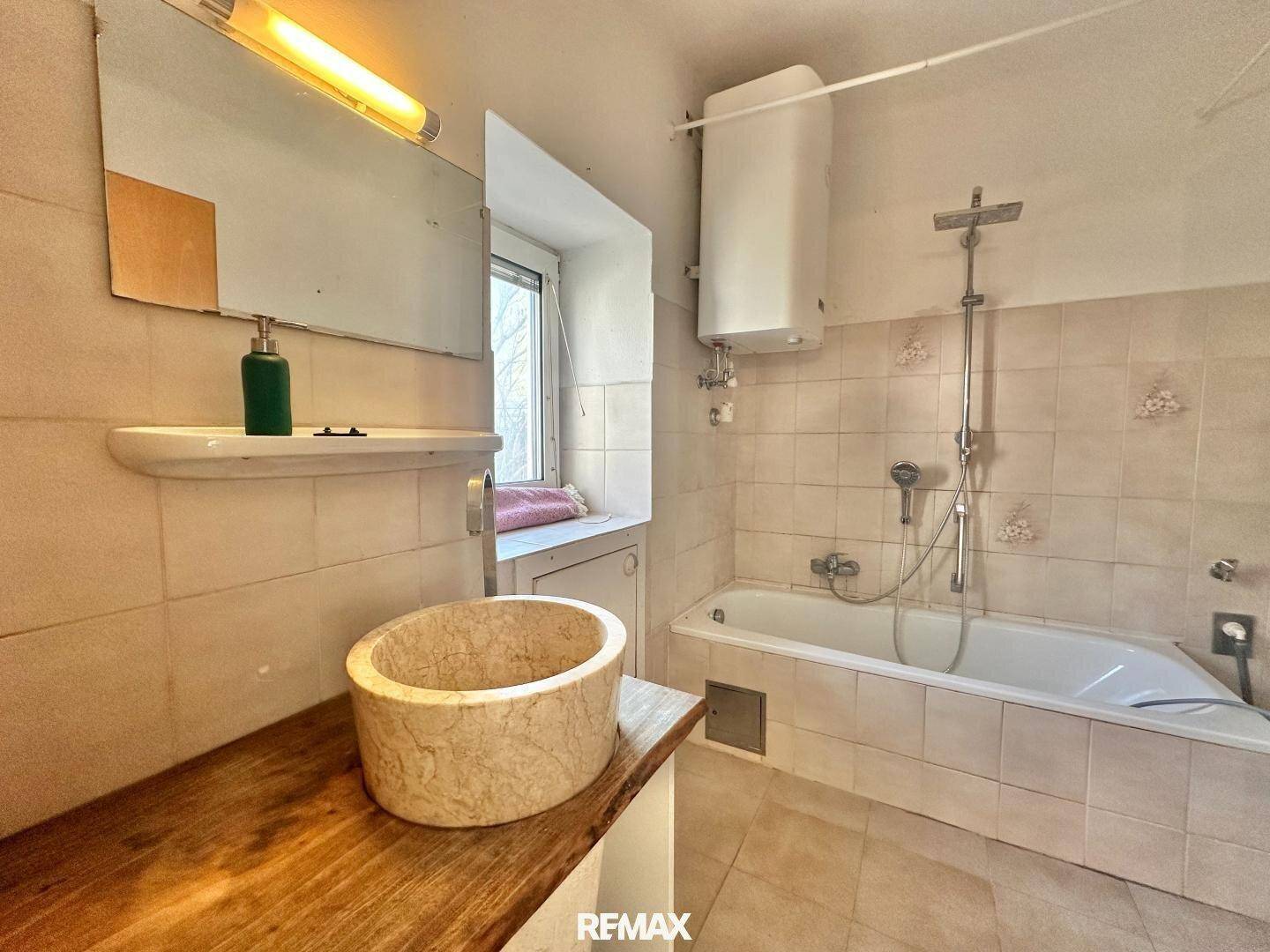 Badezimmer mit Badewanne, einem Waschbecken auf Holzplatte und Fliesen an den Wänden.