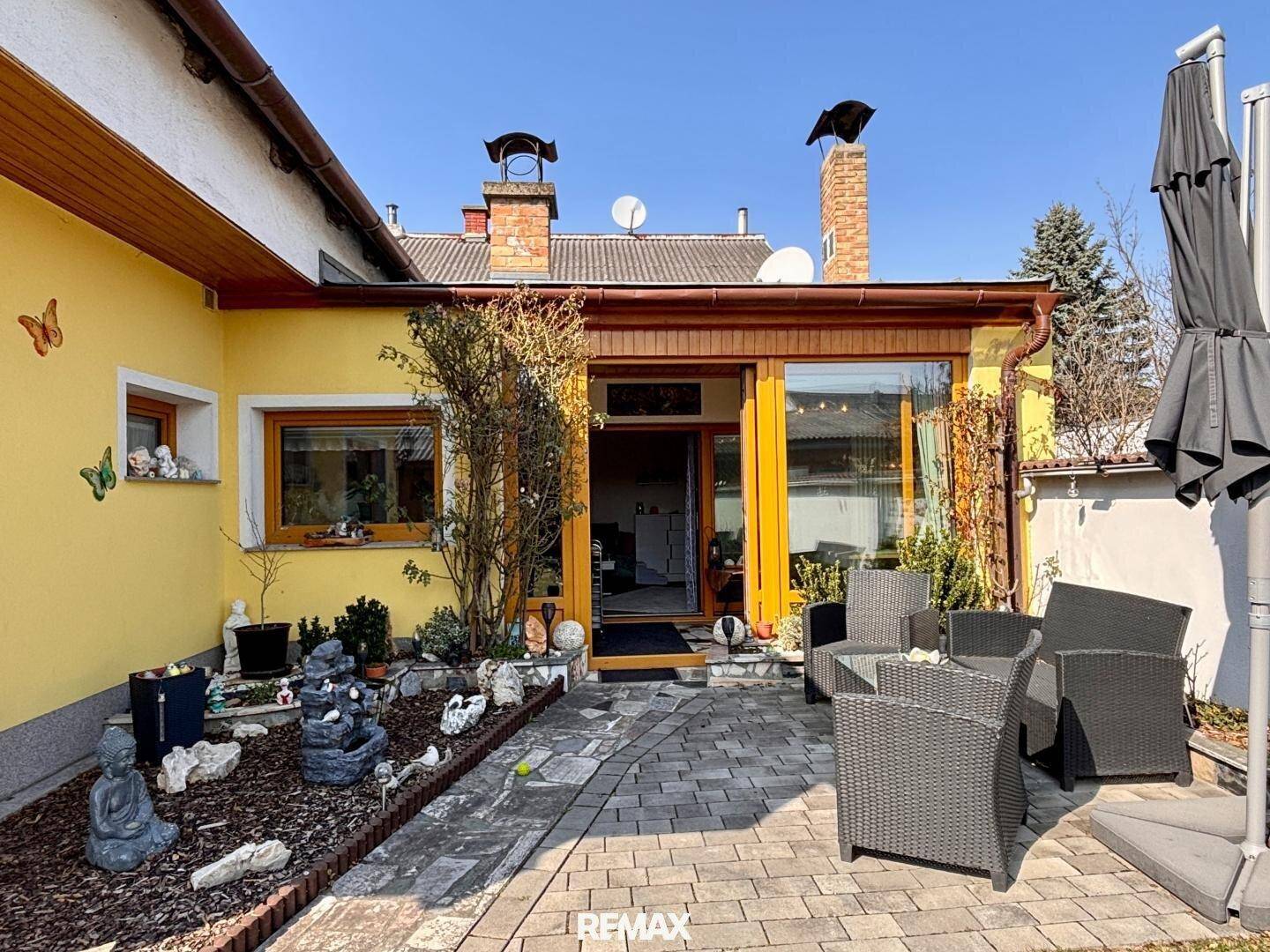 Gepflasterte Terrasse mit Gartenmöbeln und Blumenbeeten.