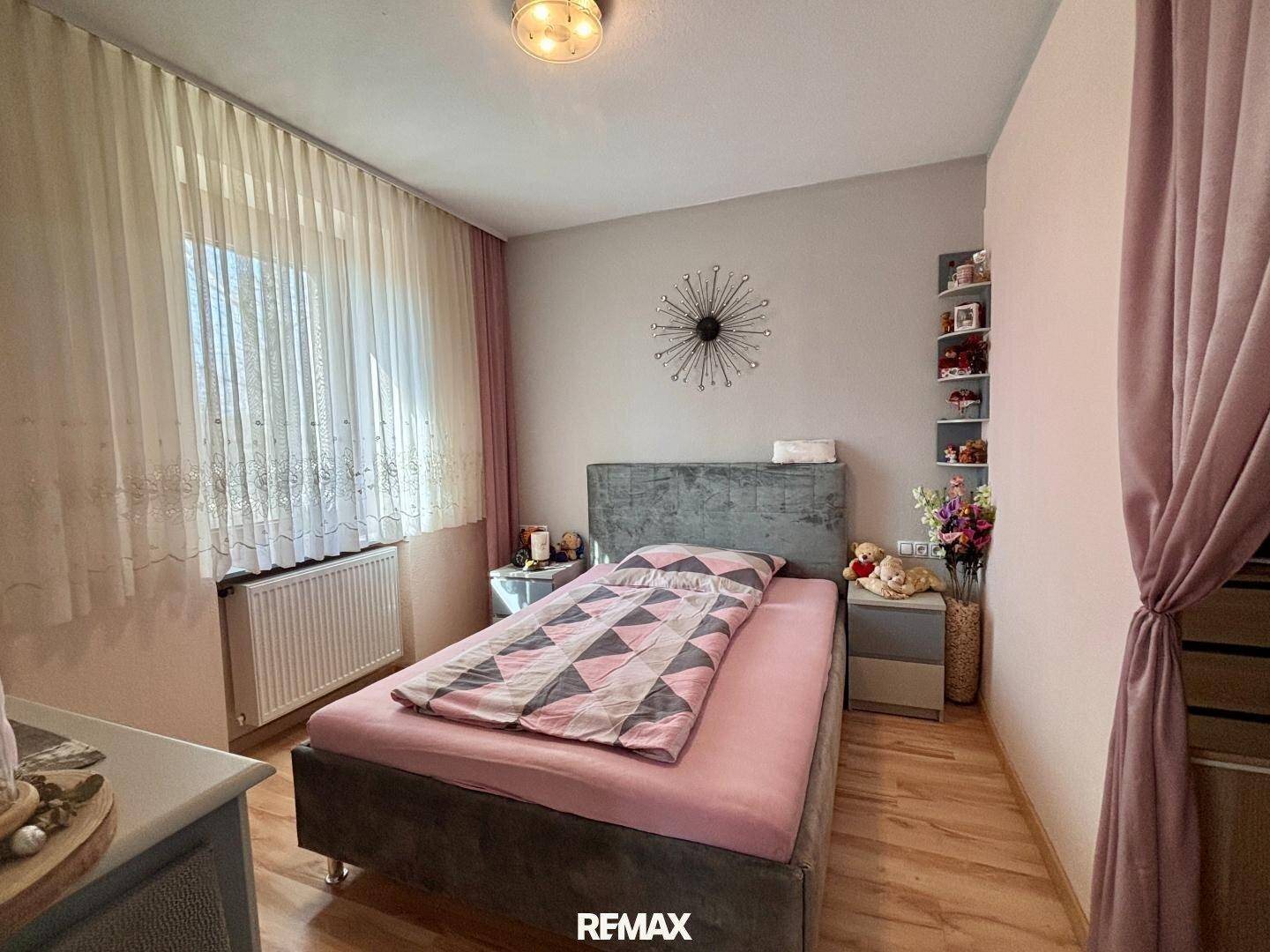 Schlafzimmer mit Einzelbett, Heizkörper und Vorhängen in Pastelltönen.