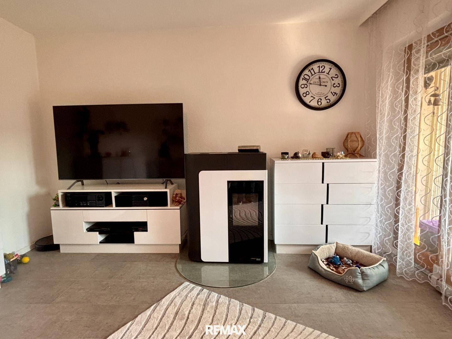 Moderner Kaminofen im Wohnzimmer mit Fliesenboden und großem Fernseher.