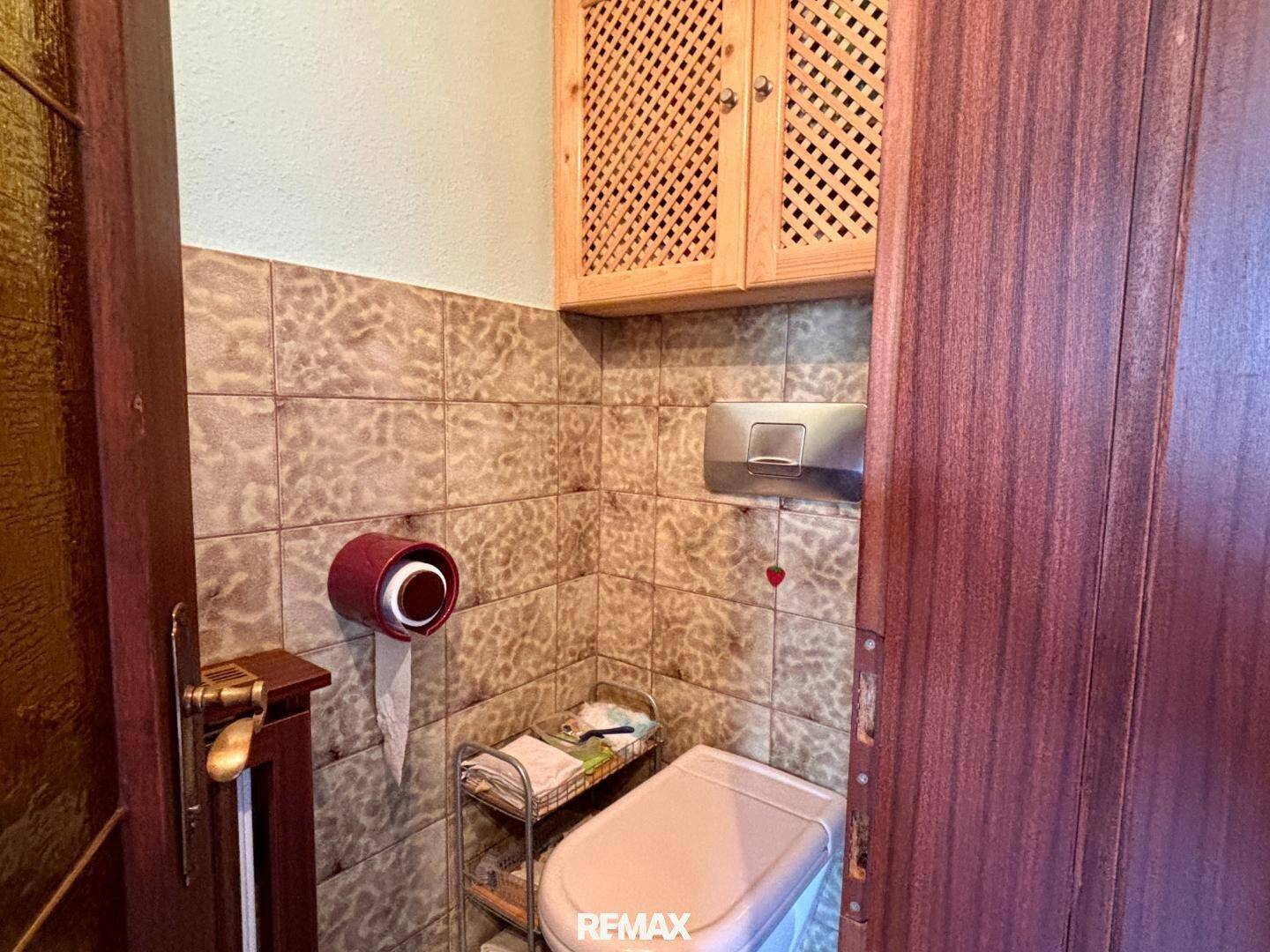 Separate Toilette mit Fliesen, Wand-WC und Holzschrank.
