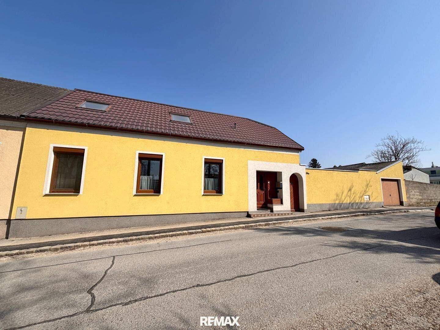 Gelbes Haus mit braunem Ziegeldach und einfacher Fassade, von der Straße aus gesehen.