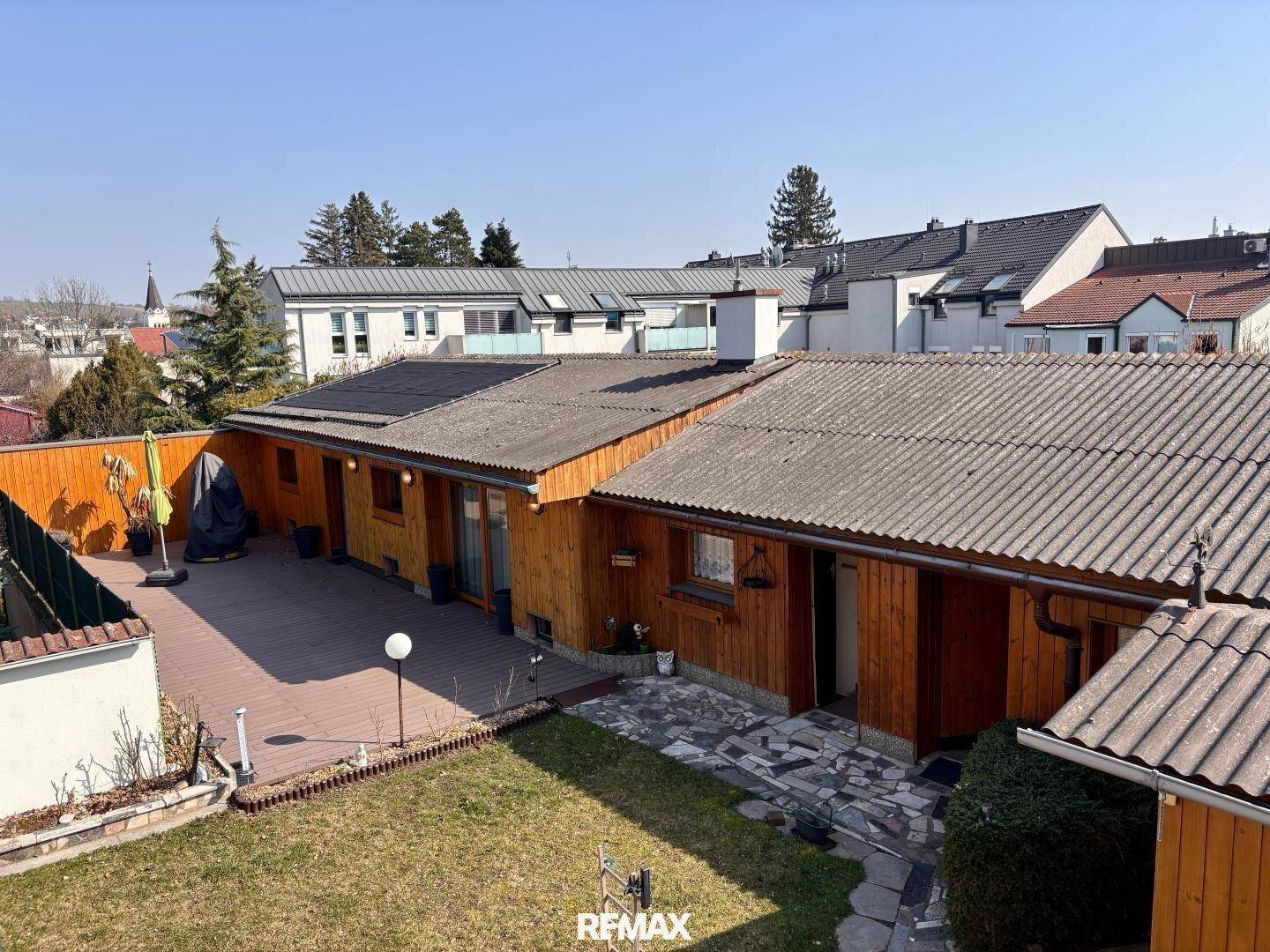Hinterhof mit Holzterrasse, Rasenfläche und Blick auf die Umgebung.