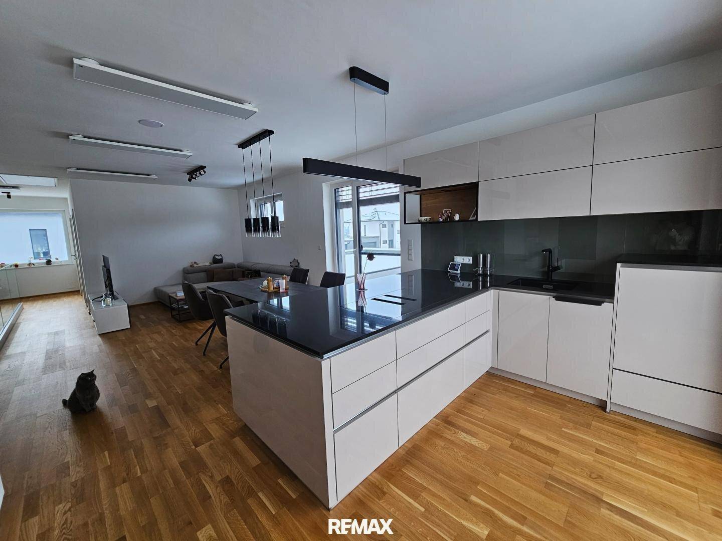Moderne offene Küche mit Kochinsel, dunkler Arbeitsplatte und Holzboden im Wohnbereich.
