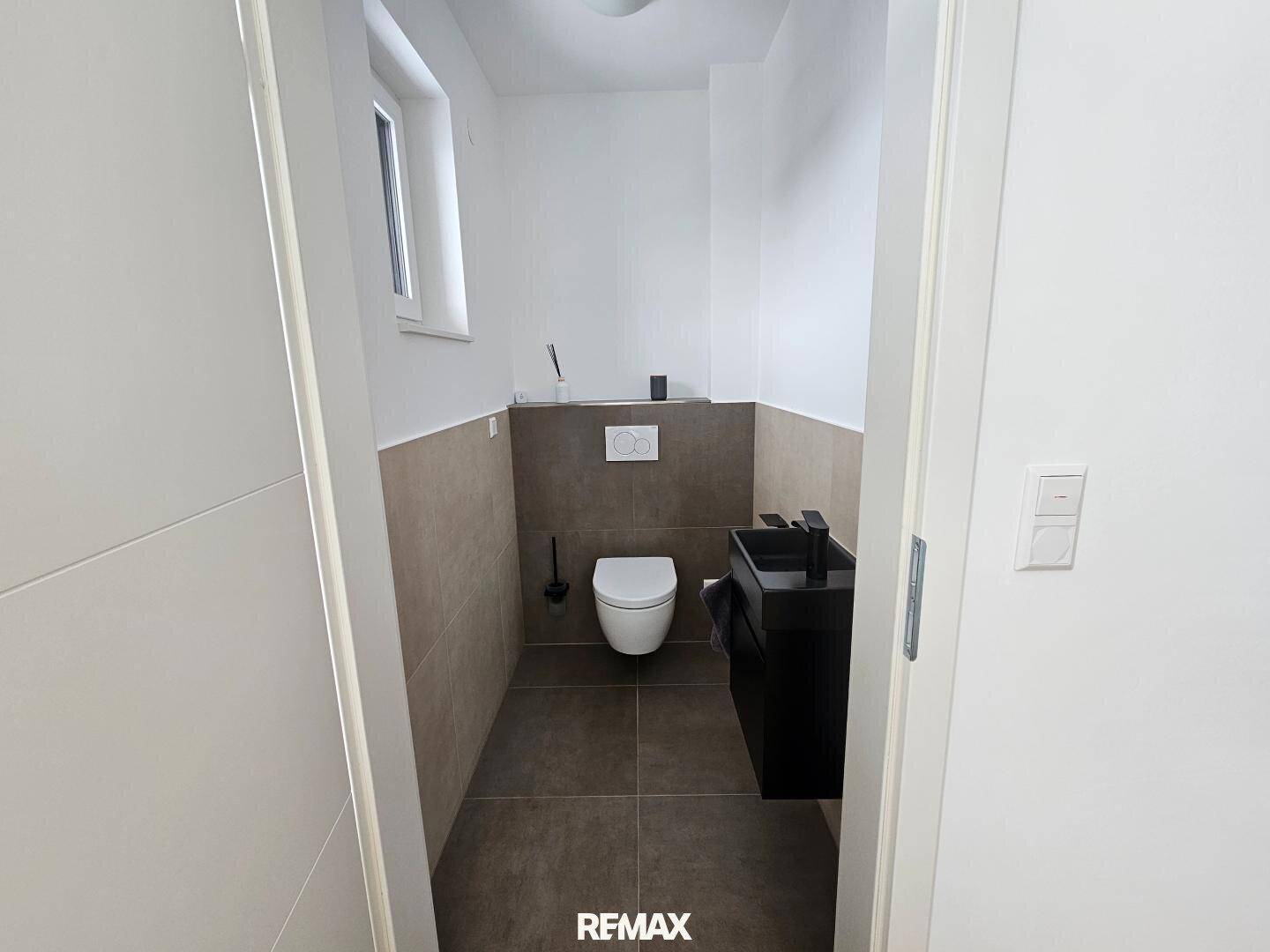 Kleines, modernes Gäste-WC mit Wand-WC, schwarzem Waschbecken und Fenster.