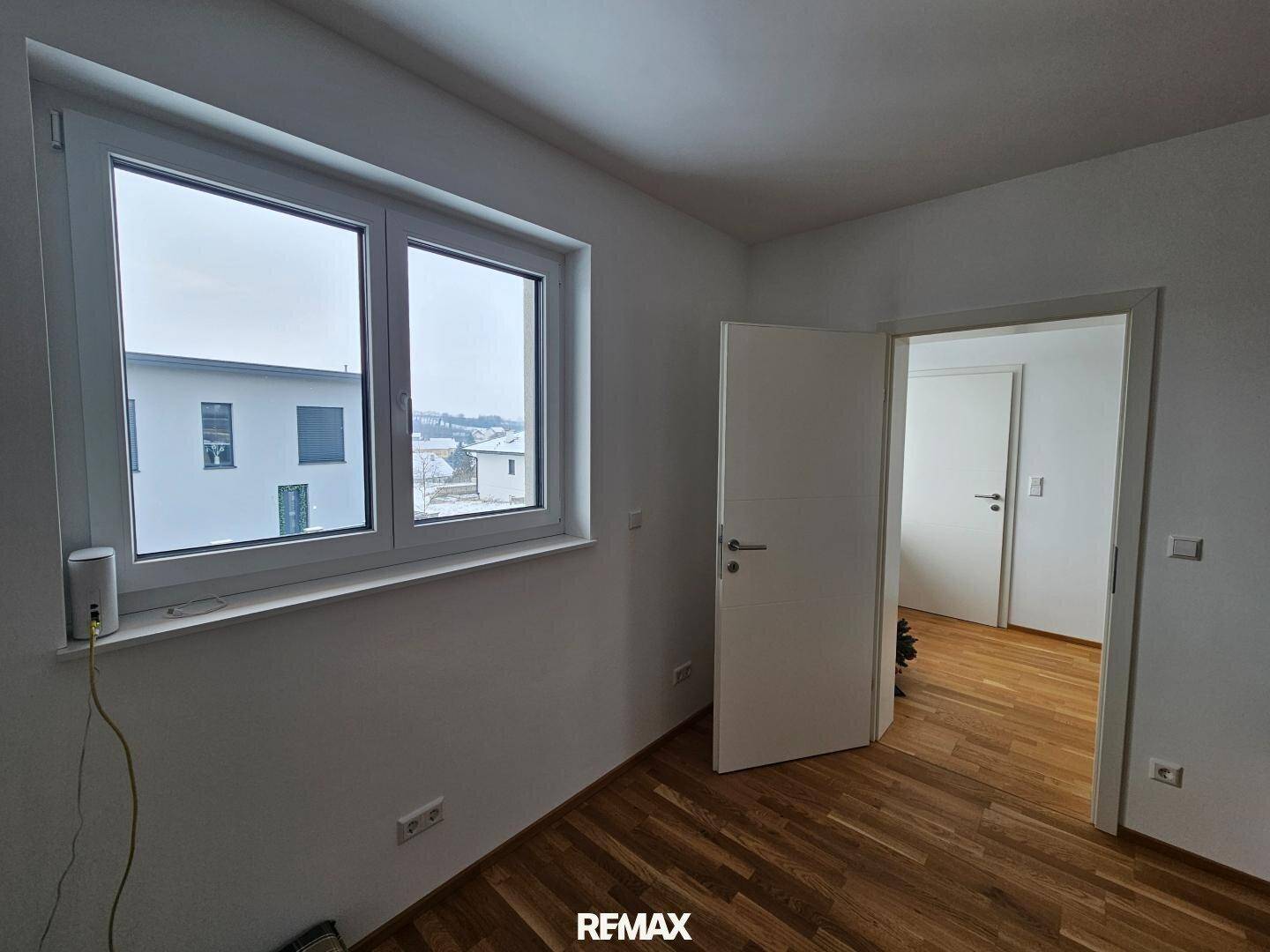 Helles Schlafzimmer mit Holzboden und großem Fenster mit Blick ins Grüne.