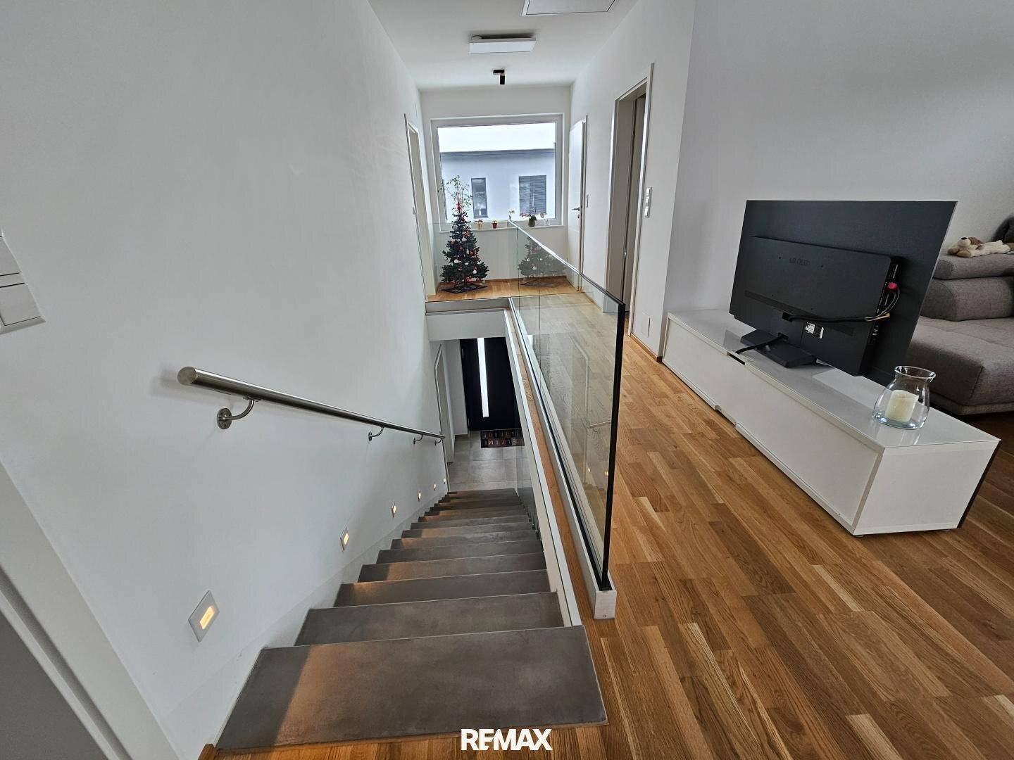 Heller Eingangsbereich mit moderner Treppe, Glasgeländer und hochwertigem Holzboden.