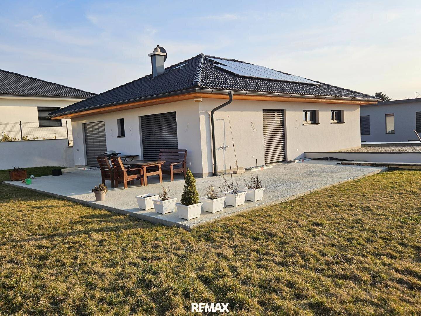Modernes Haus mit Solaranlage und einer möblierten Terrasse, umgeben von einem gepflegten Rasen.