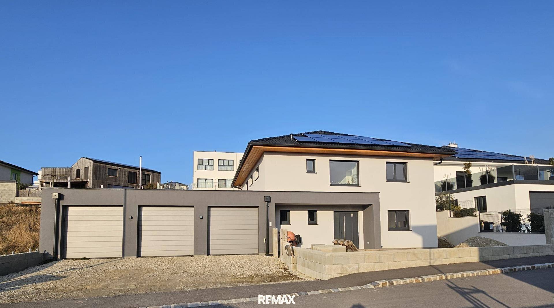 Neubau-Einfamilienhaus mit integrierter Doppelgarage und Solarpaneelen auf dem Dach.